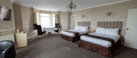 A hotel room with two beds, a desk, a chair, a TV, and a chandelier.