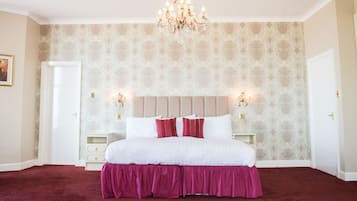 A bedroom with a large bed, a chandelier, and patterned wallpaper.