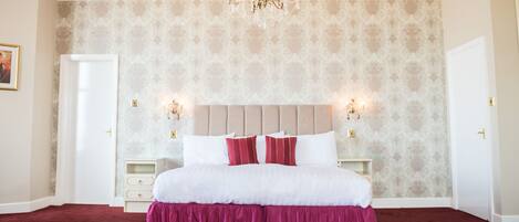 A bedroom with a large bed, a chandelier, and patterned wallpaper.