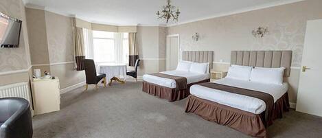 A hotel room with two beds, a desk, a chair, a TV, and a chandelier.