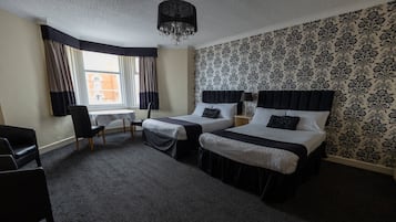 A hotel room with two beds, a desk, a chair, and a window with curtains.