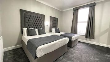 A hotel room with two beds, grey headboards, and a large window with curtains.