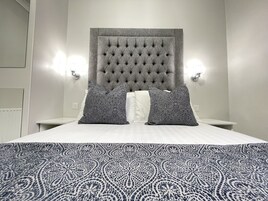 Een net opgemaakt bed met een geborduurde hoofdbord, twee gestreepte kussens en een gestreept beddegoed.