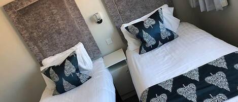 Two single beds with matching headboards and pillows, a small bedside table, and a power outlet on the wall.