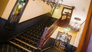 A grand staircase with ornate railings and a chandelier, leading to an upper floor.
