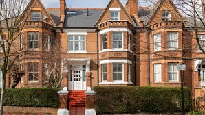 Un edificio tradicional de ladrillo con entrada en esquina, varias ventanas y una chimenea destacada.