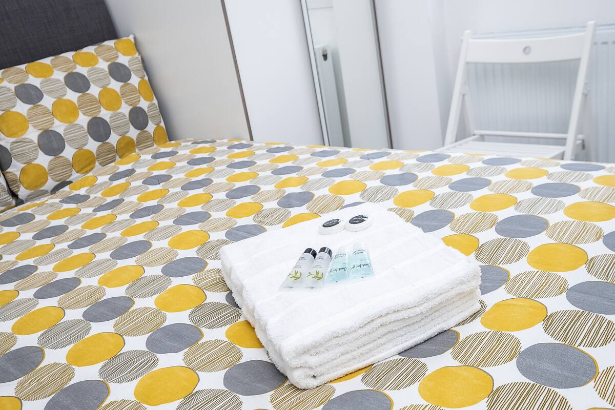 Una cama bien hecha con una colcha estampada, una toalla blanca doblada y un juego de artículos de aseo sobre la cama.