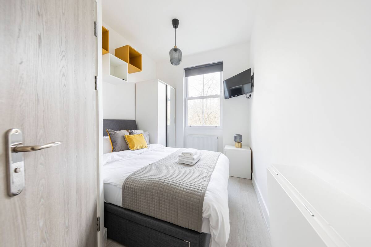 Un dormitorio moderno con cama, mesita de noche, televisor y ventana.