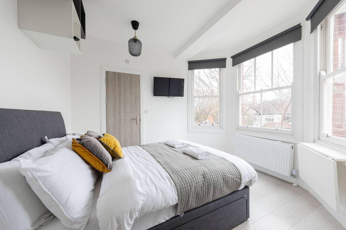 Un dormitorio moderno con cama, televisión, ventana y radiador.