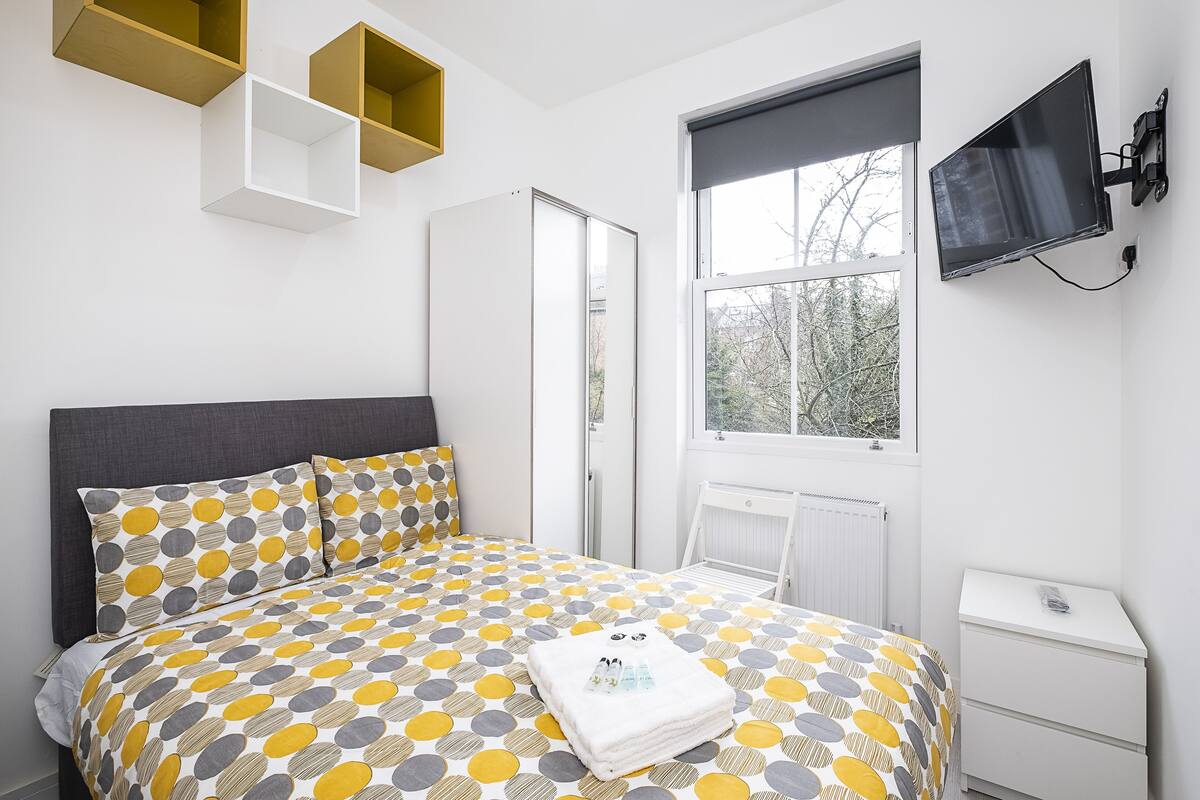 Un dormitorio con cama, armario, televisor y ventana.