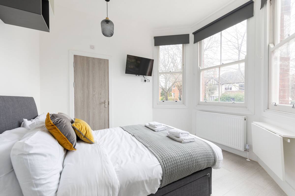 Un dormitorio con cama, televisor, ventana y radiador.