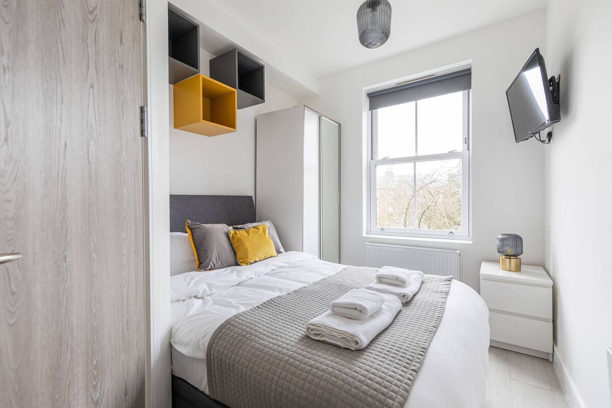 Un dormitorio moderno con cama, mesitas de noche, televisión y ventana.