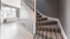 Una escalera con barandilla blanca y escalones cubiertos de alfombra a rayas.