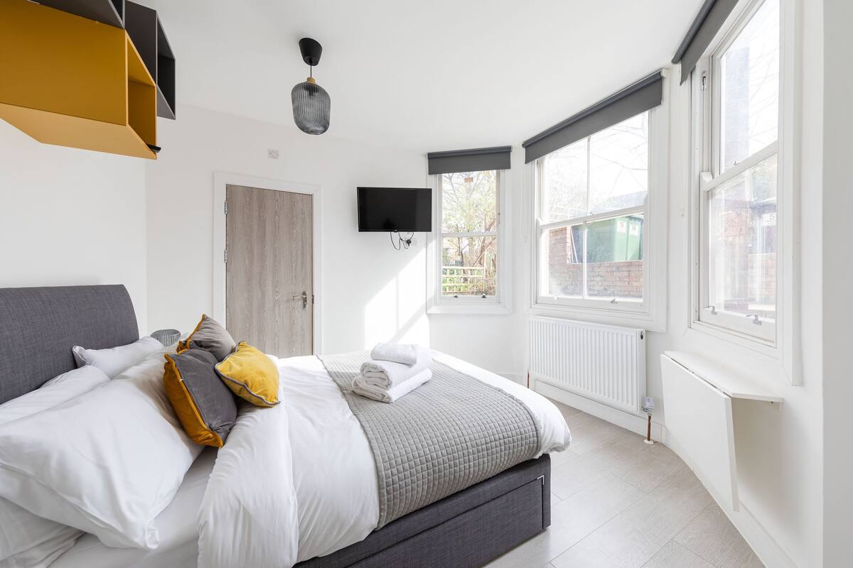 Un dormitorio moderno con cama, televisión y ventanas amplias.