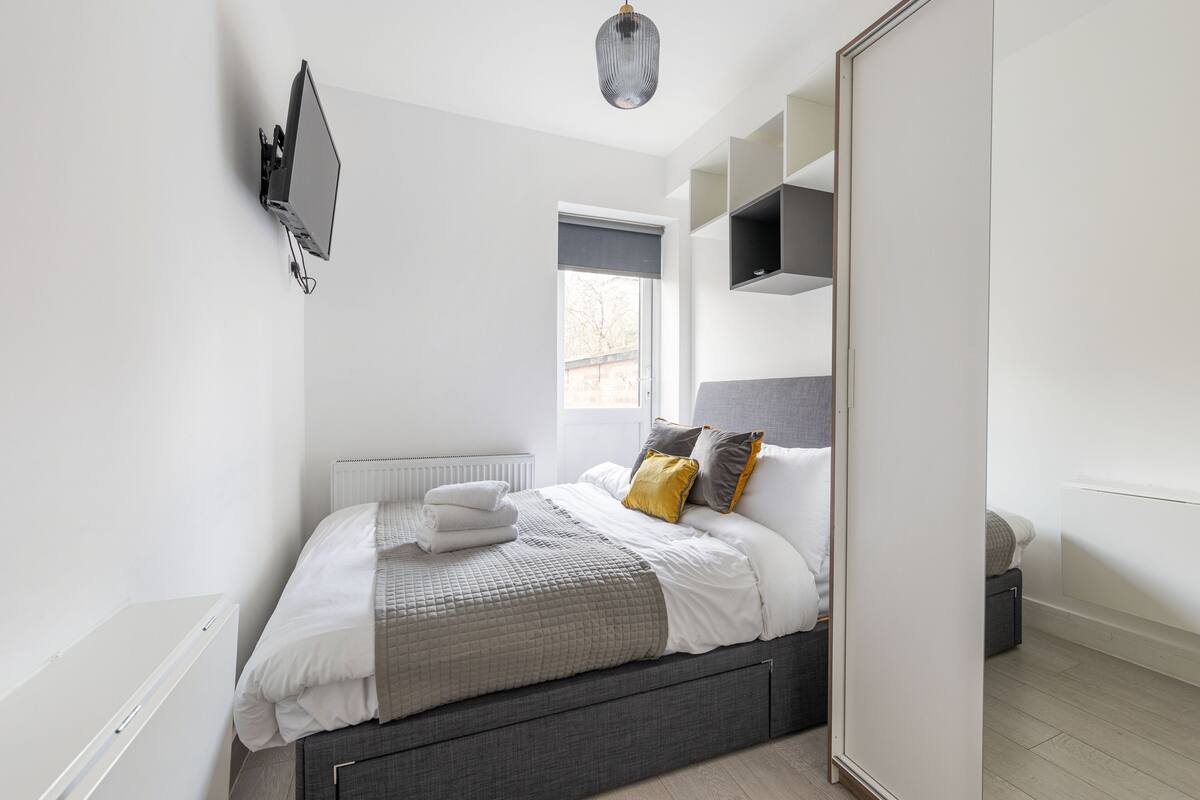 Un dormitorio moderno con cama, televisor montado en la pared y estanterías empotradas.