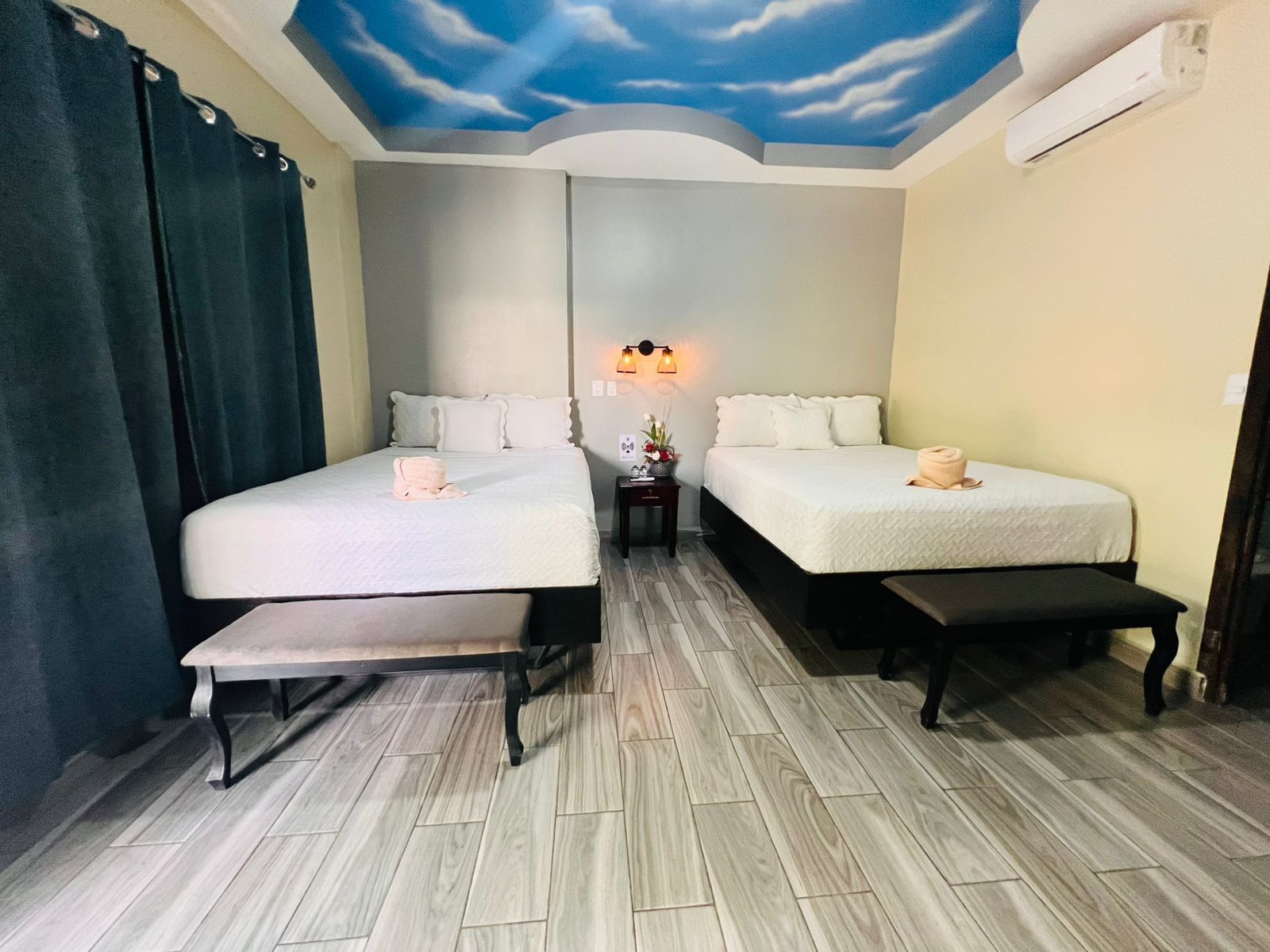 Ein Hotelzimmer mit zwei Betten, einer Bank, einem Deckenfresko und einem Nachttisch mit Lampe.