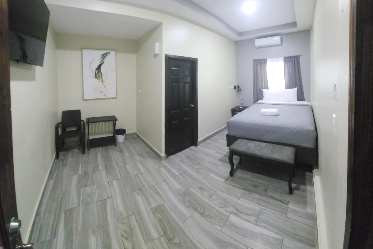 A hotel room with a bed, a bench, a chair, a wall-mounted TV, and a painting.
