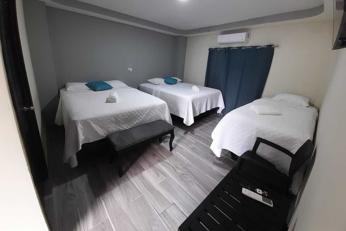 A hotel room with three beds, a bench, and an air conditioning unit.