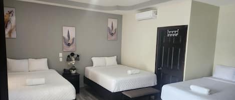 Habitación de hotel con tres camas, piso de madera y unidad de aire acondicionado en la pared.