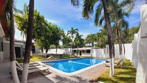 A swimming pool surrounded by palm trees and lounge chairs, with a clear blue sky above. - Mi Tierra Aeropuerto Hotel y Restaurante (San Luis Talpa)
