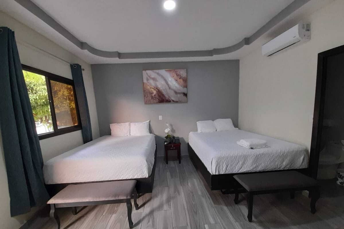 A hotel room with two beds, a bench, a small table, and a painting on the wall.
