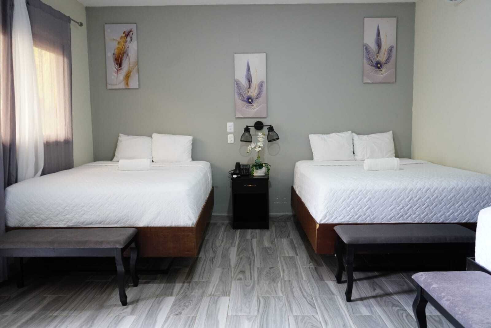 Une chambre d’hôtel avec deux lits, une petite table, un banc et des œuvres d’art accrochées aux murs.
