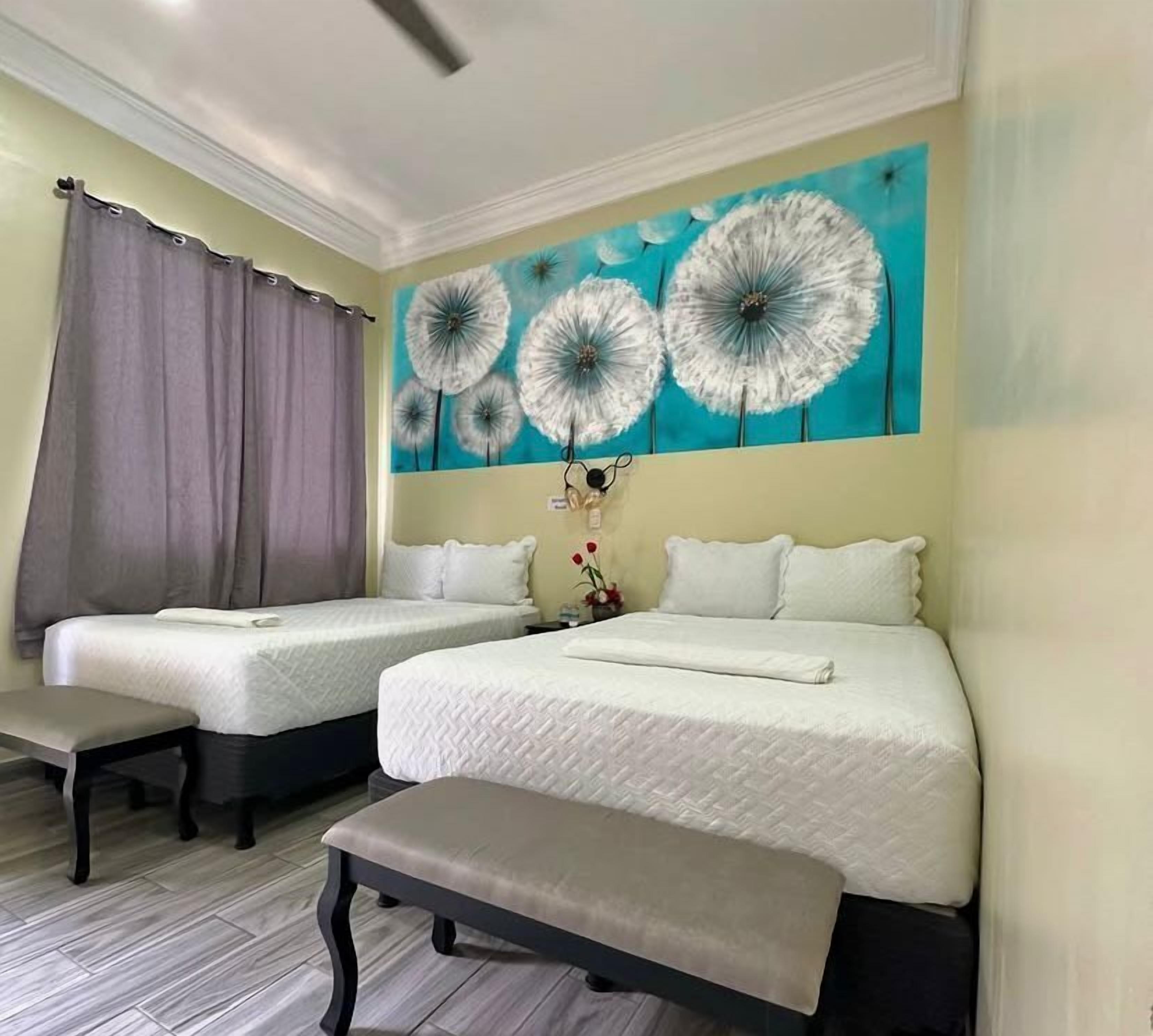 A hotel room with two beds, a bench, and a dandelion-themed wall mural.
