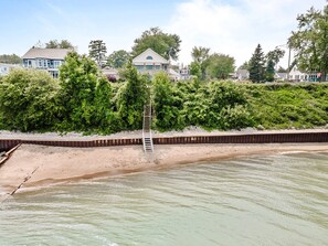 A beach with a wooden ladder leading to a wooden platform, surrounded by dense greenery and houses in the background. - Private Beach, Bonfire, New Blackstone Grill (Lexington)