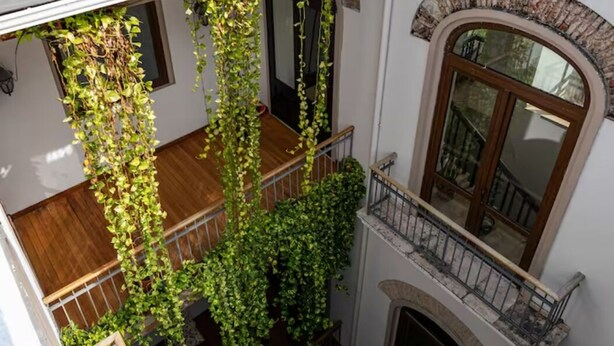 Un interior de varios niveles con una escalera de madera, un balcón con barandilla de hierro forjado y un amplio ventanal de arco.