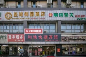 Un immeuble à plusieurs étages abritant divers commerces au rez-de-chaussée, notamment une pharmacie, une boulangerie et un restaurant.