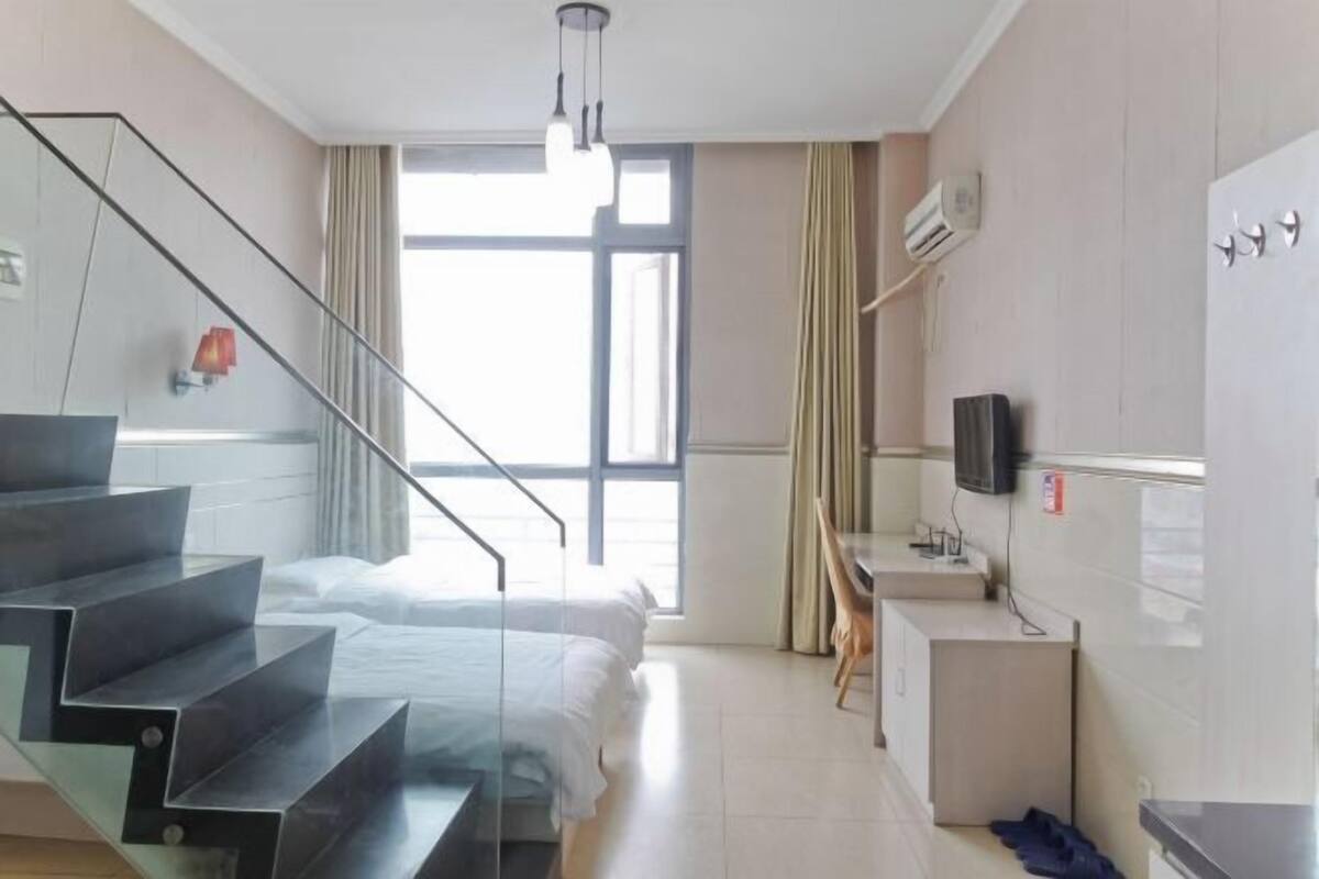 A hotel room with a bed, a desk, a TV, a staircase, and a window.