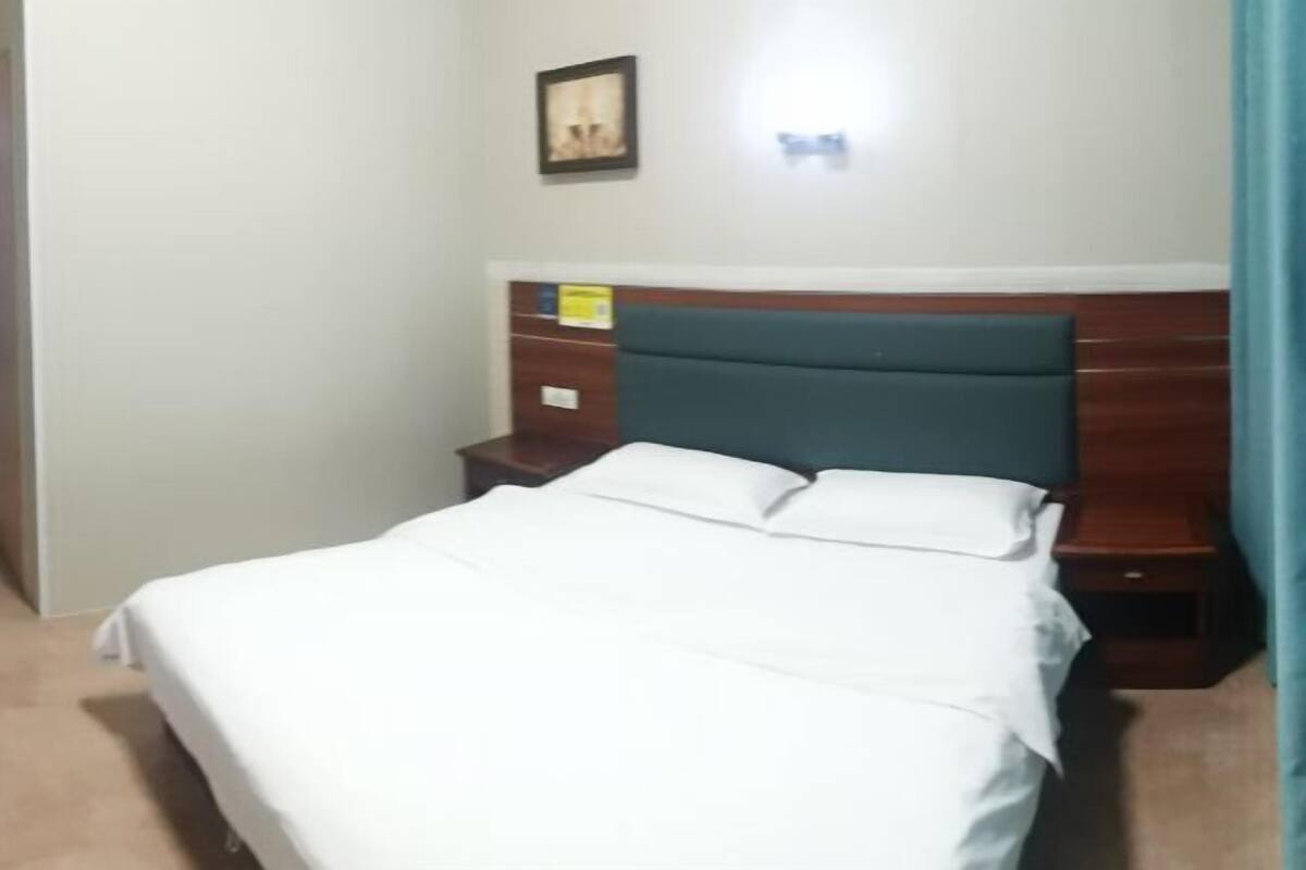 A hotel room with a bed, wooden headboard, nightstands, and a wall-mounted light fixture.