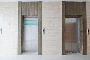 Twee liftdeuren in een hal met een betegelde vloer en een structuurwand.