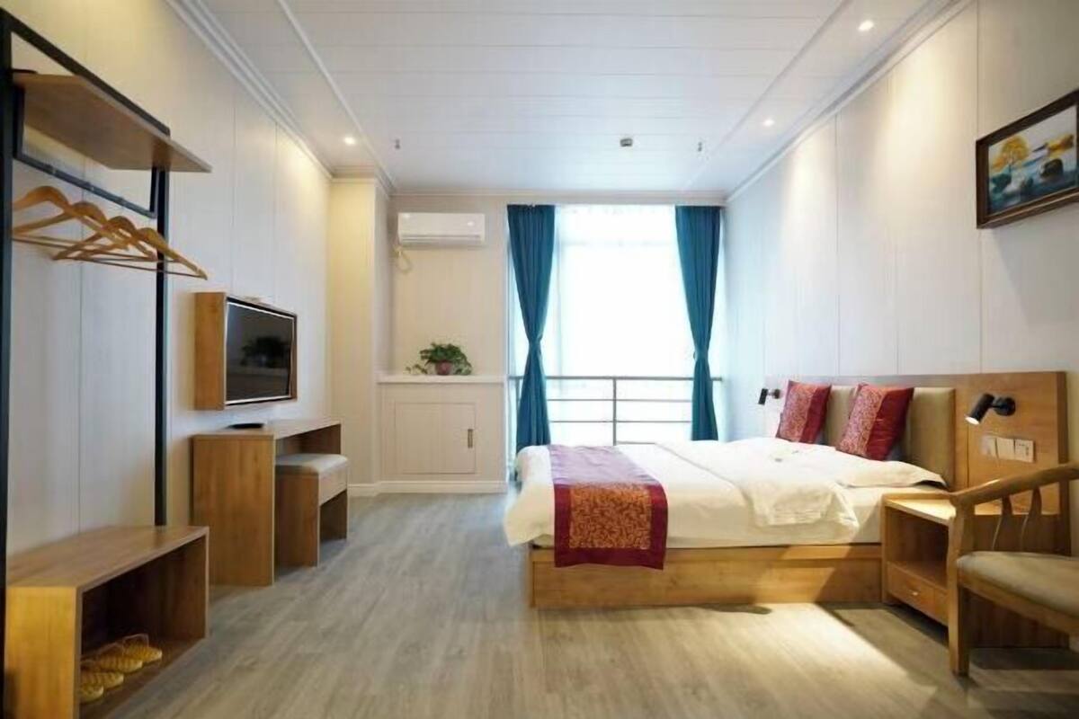 A modern hotel room with a bed, TV, wooden furniture, and a window with curtains.