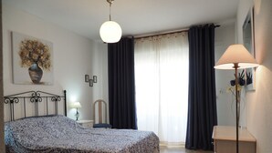 Ett sovrum med en säng, ett sängbord, en lampa, en stol, en byrå och ett fönster med gardiner.