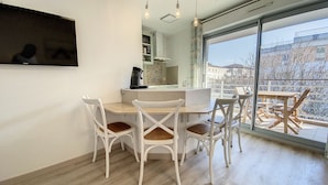 A dining area with a round table and white chairs, a coffee maker, and a view of a balcony with outdoor furniture.