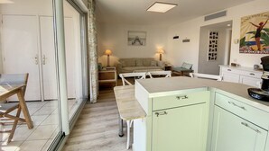 A room with a kitchenette, a dining table, a sofa, and a large window with curtains.