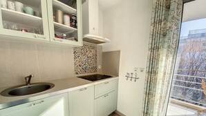 A kitchen with a sink, cabinets, a stove, and a window with a view of trees.