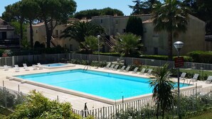 A rectangular swimming pool with a white fence, surrounded by lounge chairs and palm trees. - Appartement with terrace, wifi, parking (Agde)