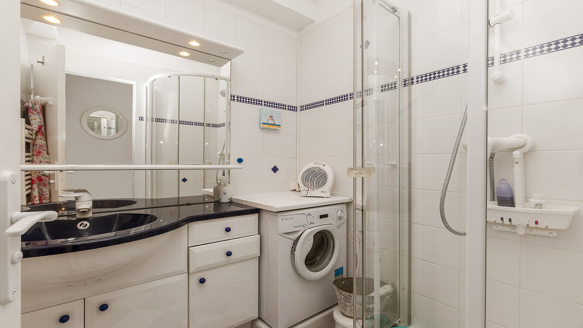 A bathroom with a washing machine, a sink, a mirror, and a shower enclosure.