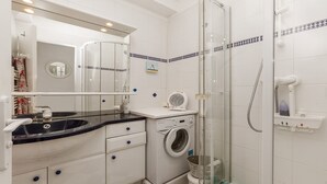 Een badkamer met een wasmachine, een wastafel, een spiegel en een douchecabine.