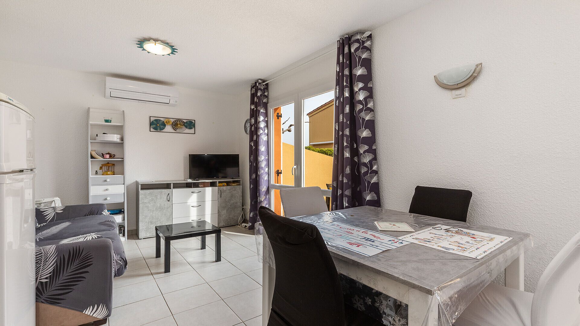 A compact living space with a dining table, chairs, a sofa, a TV, and a kitchen area.