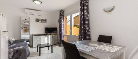 A compact living space with a dining table, chairs, a sofa, a TV, and a kitchen area.