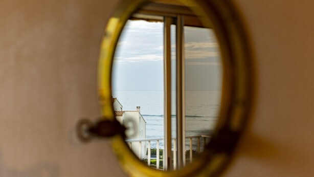 A view through a window with a metal frame, overlooking a body of water and a building with a white facade. - Studio 4 ppl, sea view balcony, pool, parking (Agde)