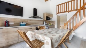 A modern kitchen with wooden cabinets, a dining table with chairs, a built-in microwave, and a staircase.