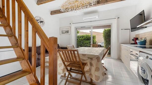 A modern kitchen with a dining area, wooden staircase, and a view of the outside.
