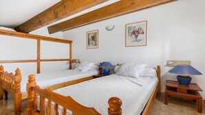 A room with two wooden beds, a wooden bench, a small table with a lamp, and two framed pictures on the wall.