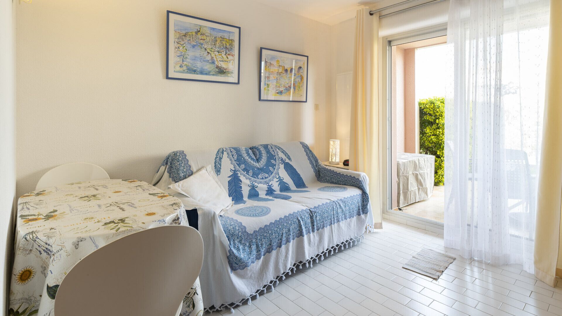 A cozy room with a sofa and a table, a balcony with a table, and two framed artworks on the wall.