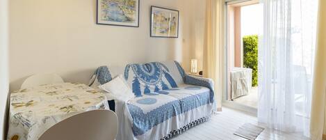 A cozy room with a sofa and a table, a balcony with a table, and two framed artworks on the wall.