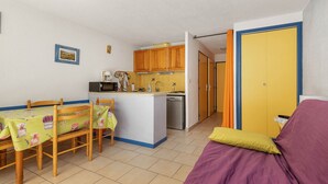 A compact kitchen with wooden cabinets, a dining table with chairs, a sofa, and a small island with a sink and microwave.